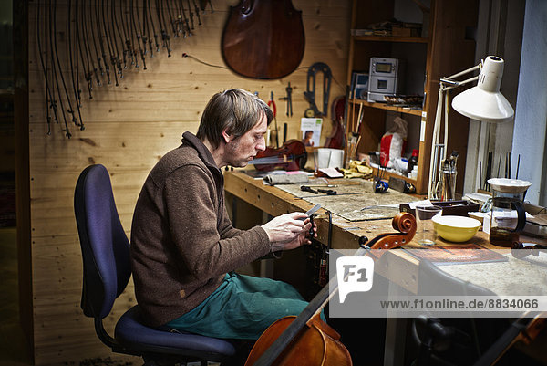 Violin maker in his workshop filing a cello mechanism
