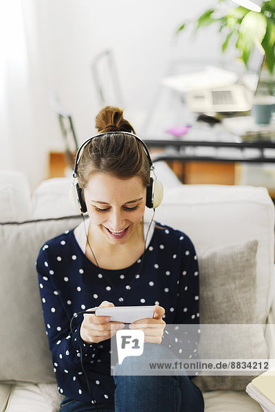 Junge Frau spielt zu Hause Videospiele mit Smartphone