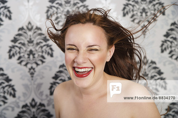 Porträt einer lachenden jungen Frau vor karierter Tapete