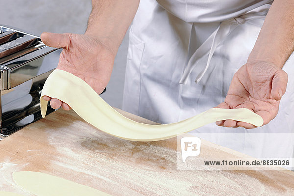 Hände eines Mannes mit ausgerolltem Nudelteig für hausgemachte Tortelloni