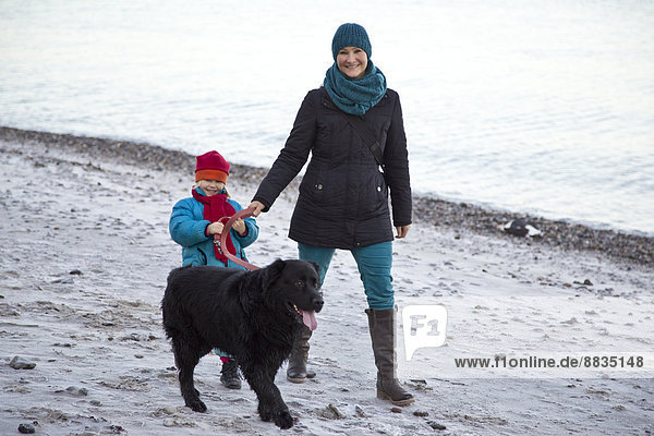 Germany  Schleswig-Holstein  Kiel  mother and daughter walking with labrador along the beach