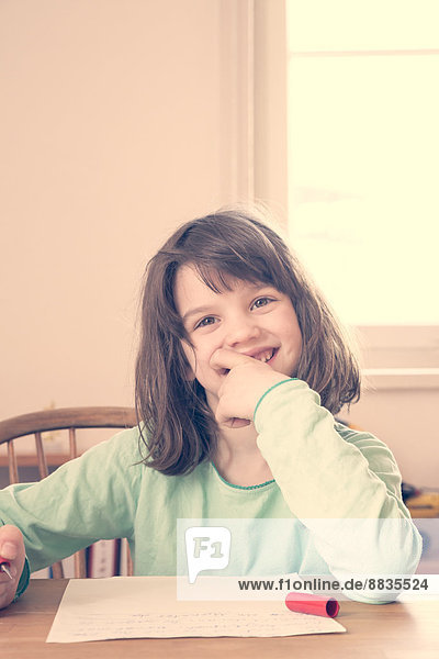 Porträt eines lächelnden kleinen Mädchens bei den Hausaufgaben