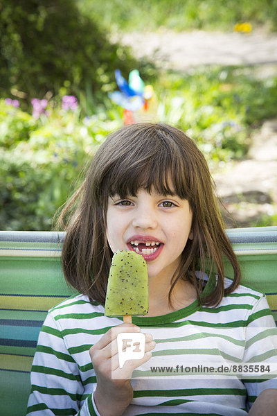 Porträt eines Mädchens mit Zahnlücke  das Kiwi-Eis-Lolly hält