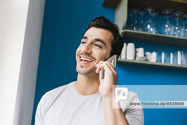 Portrait of laughing young man telephoning with smartphone in his kitchen