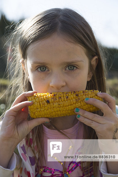 Porträt eines kleinen Mädchens beim Essen von gegrilltem Maiskolben