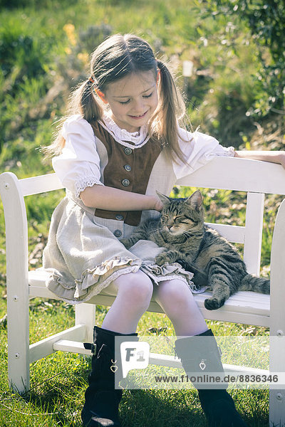 Portait of little girl sitting on wooden bench with cat
