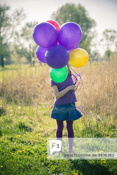 Kleines Mädchengesicht versteckt hinter Luftballons