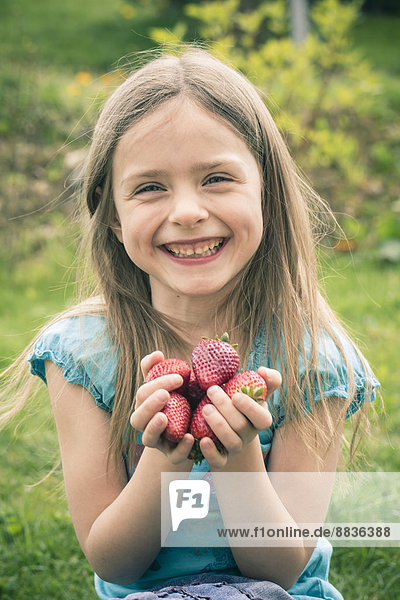 Porträt eines lächelnden kleinen Mädchens mit einer Handvoll Erdbeeren