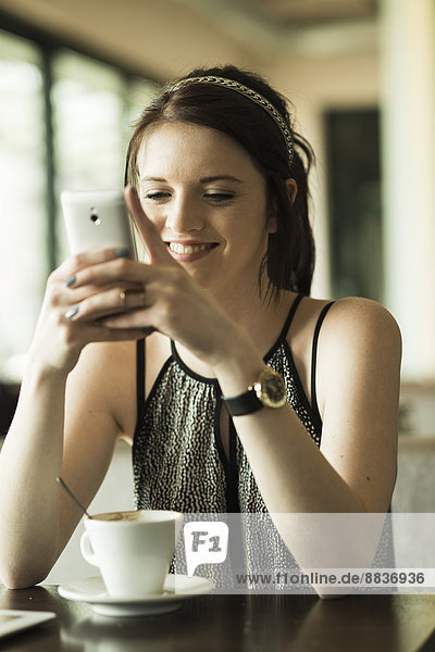Porträt einer jungen Frau mit Smartphone im Café