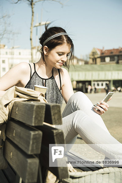 Portrait of young woman with coffee to go using smartphone