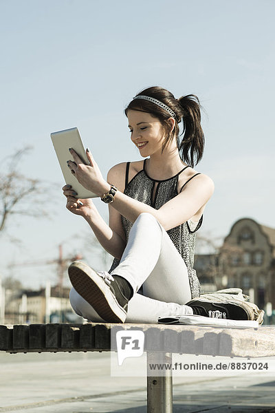 Junge Frau mit Tablet-Computer auf einer Bank sitzend
