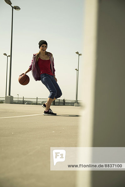 Junge Frau spielt Basketball im Freien