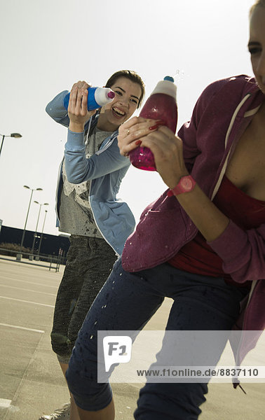 Zwei verspielte junge Frauen  die mit einer Wasserflasche spritzen.