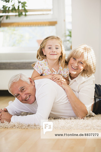 Family portrait of senior couple and granddaughter lying on the floor at home