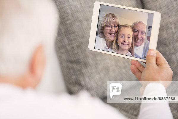 Senior betrachtet digitales Tablett mit Familienporträt