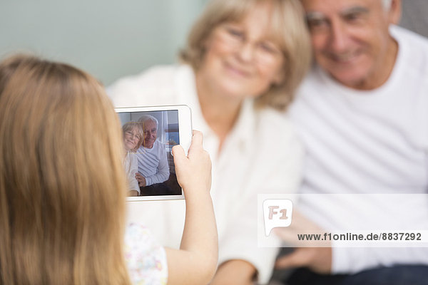 Kleines Mädchen fotografiert ihre Großeltern mit digitalem Tablett zu Hause.