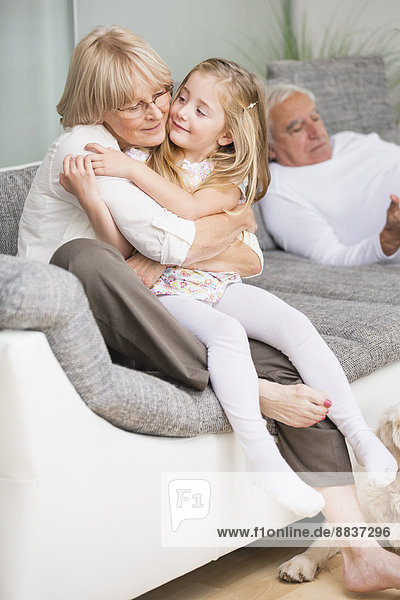 Portrait of senior woman hugging granddaughter on sofa in living room