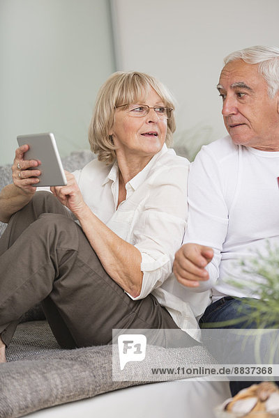 Senior couple with digital tablet side by side on sofa in living room