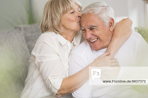 Seniorin beim Küssen ihres Mannes im Wohnzimmer