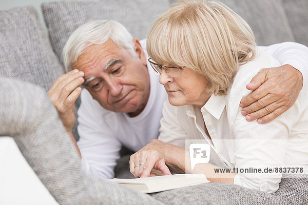Senior couple with book lying side by side on sofa