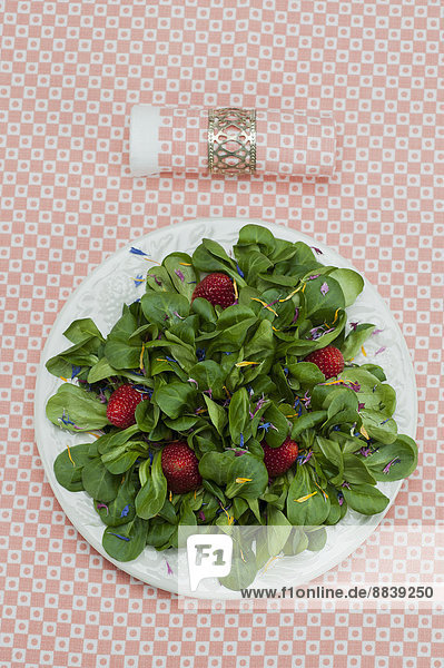 Feldsalat mit Erdbeeren und Blütenblättern angerichtet auf einem Teller  Serviette