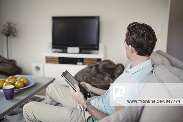 Side view of man with digital tablet sitting on sofa at home