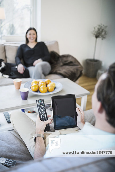 Mann mit digitalem Tablett im Sitzen auf dem Sofa mit Frau im Hintergrund