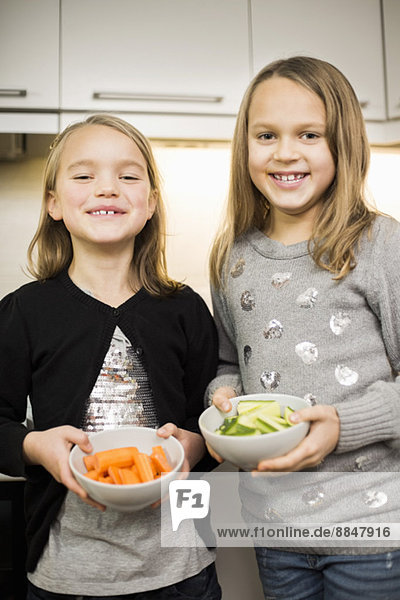 Portrait of happy sisters holding sliced vegetables in bowls at home