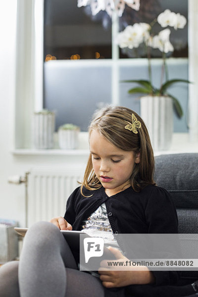Girl using digital tablet on sofa in living room