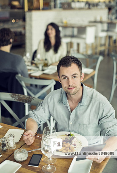 Porträt eines Geschäftsmannes mittlerer Größe mit digitalem Tablett beim Mittagessen im Restaurant