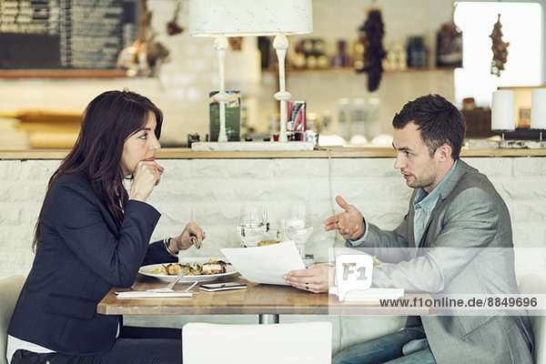 Seitenansicht eines Geschäftsmannes mit einer Kollegin  die am Restauranttisch über den Papierkram diskutiert.