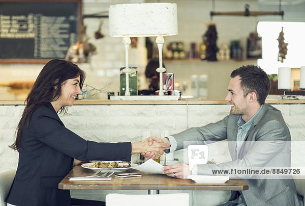 Seitenansicht des Geschäftsmannes und der Geschäftsfrau beim Händeschütteln am Restauranttisch