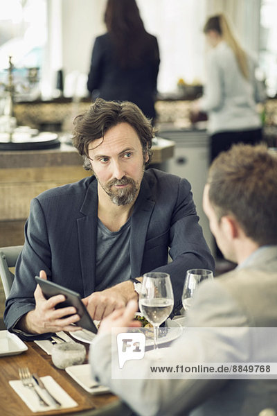 Reife Geschäftsleute diskutieren mit Kollegen am Restauranttisch über digitale Tabletts