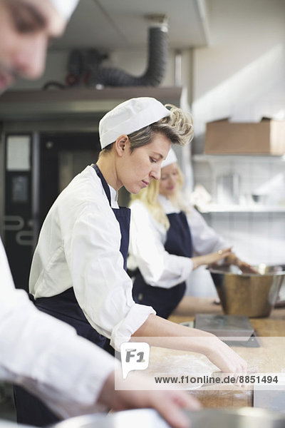 Seitenansicht der Bäckerin beim Backen mit Kollegen in der Großküche