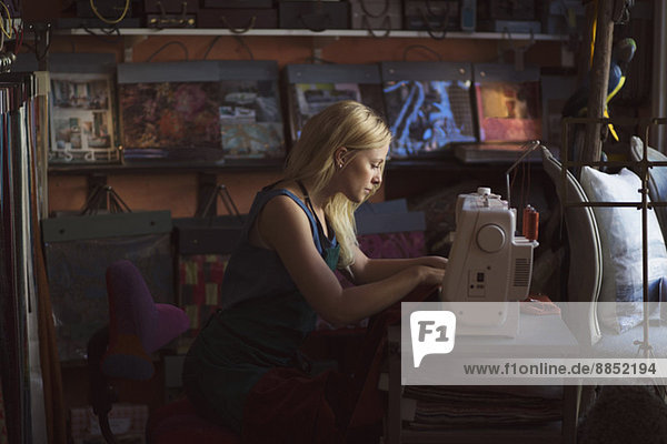 Seitenansicht der jungen Modedesignerin mit Nähmaschine im Atelier
