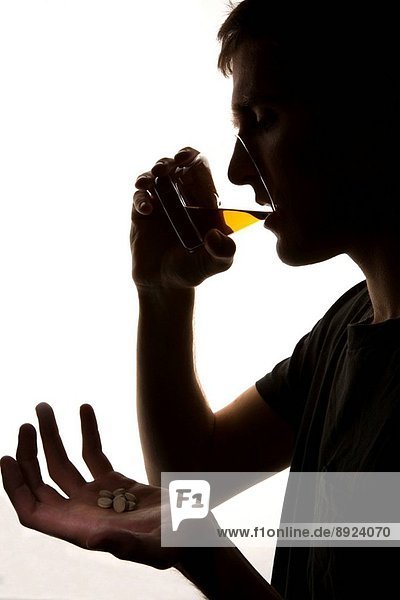 A silhouette of a depressed young man with some sleeping pills and a glass of whiskey.