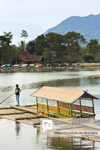 Man punting bamboo raft on Situ Cangkuang lake at this village known for its temple  Kampung Pulo  Garut  West Java  Indonesia  Southeast Asia  Asia