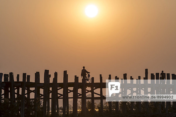 Man riding a bike on a teak bridge U Bein Bridge across Thaungthaman Lake at sunset Amarapura Mandalay Division Myanmar