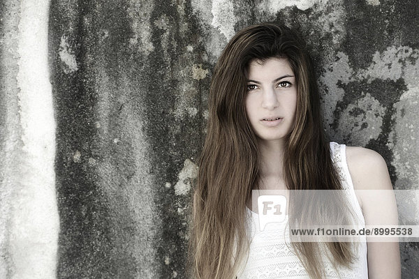 Girl with long hair  15 years  standing in front of an old weathered wall  portrait