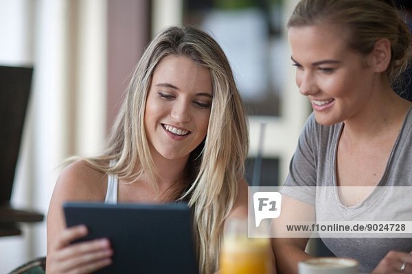 Zwei junge erwachsene Freundinnen beim Betrachten des digitalen Tabletts im Cafe