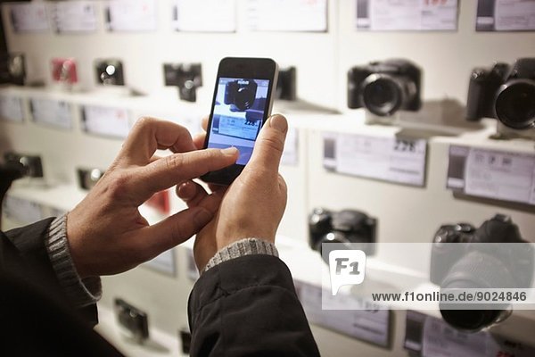 Mittlerer Erwachsener Mann fotografiert Kameras im Laden mit Smartphone
