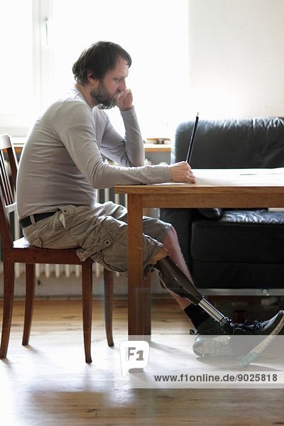 Behinderter Mann mit Laptop im Wohnzimmer