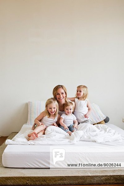 Porträt einer mittleren erwachsenen Frau im Bett mit drei Töchtern