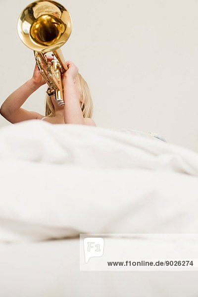 Mädchen spielt Trompete im Bett