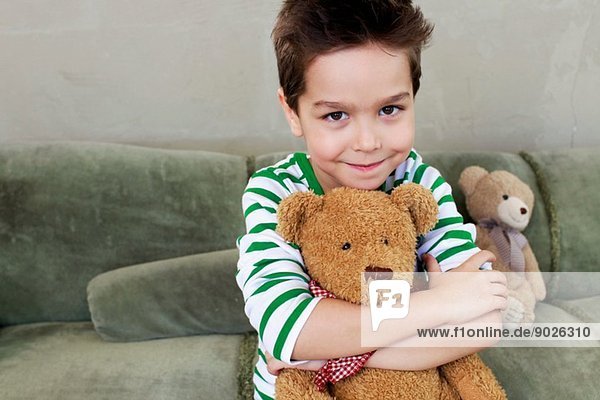 Porträt eines kleinen Jungen auf einem Sofa  der den Teddy umarmt.
