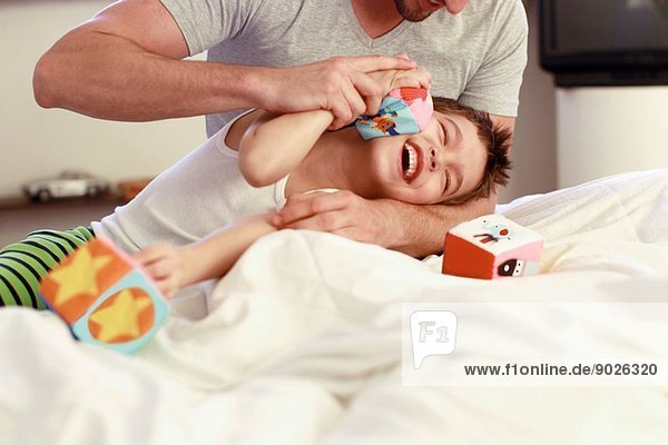 Father and young son playing with building blocks on bed