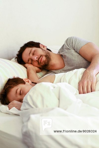 Vater und kleiner Sohn schlafen im Bett