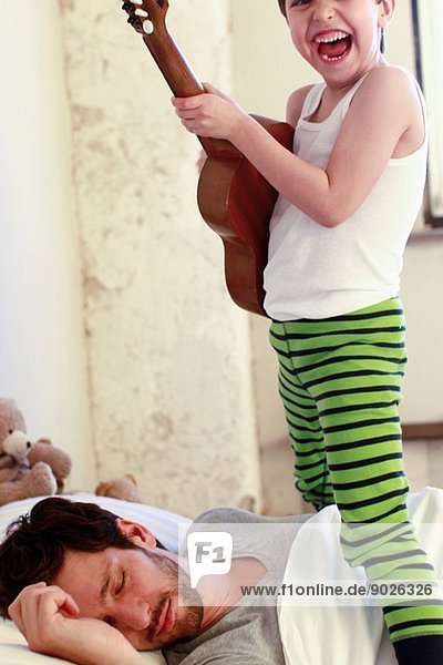 Sohn spielt Gitarre  während sein Vater schläft.