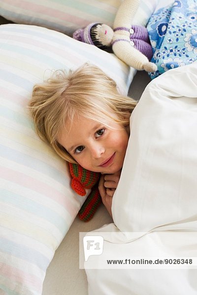 Porträt eines jungen Mädchens im Bett liegend mit Puppe