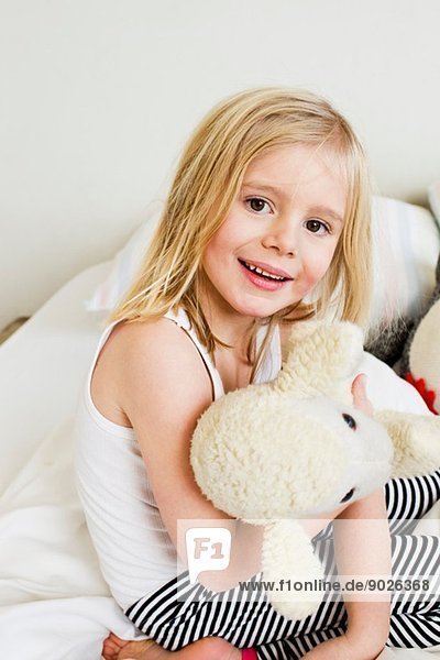 Porträt eines jungen Mädchens auf dem Bett kniend mit Plüschtier